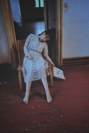 一个穿着连衣裙的年轻女子坐在木地板房间的椅子上