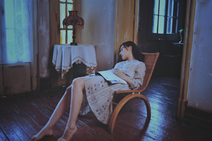 一位穿着连衣裙的年轻女士坐在有窗户的房间里的椅子上看书