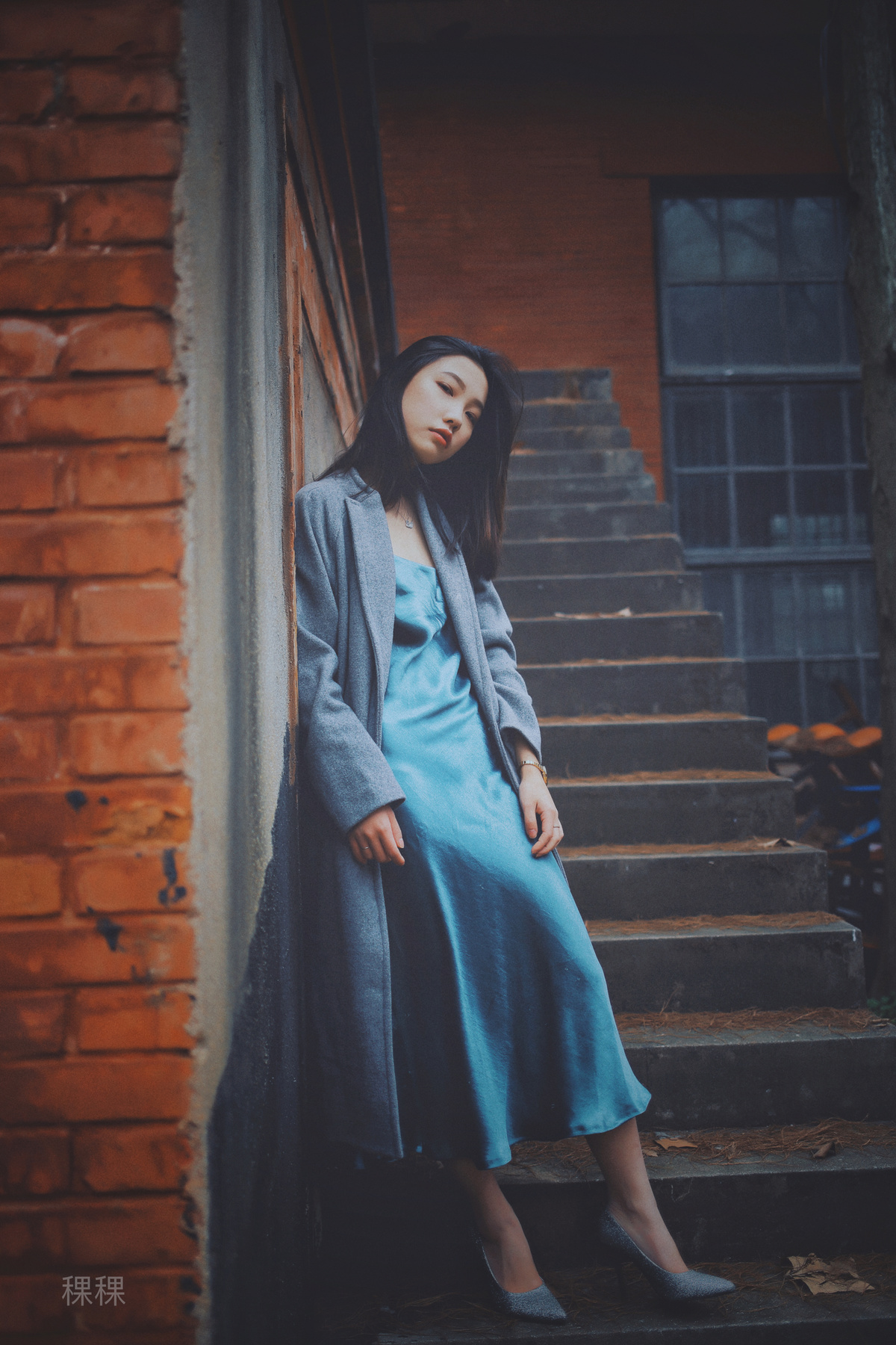 一个穿着蓝色连衣裙和外套的年轻女子坐在一所房子的台阶上
