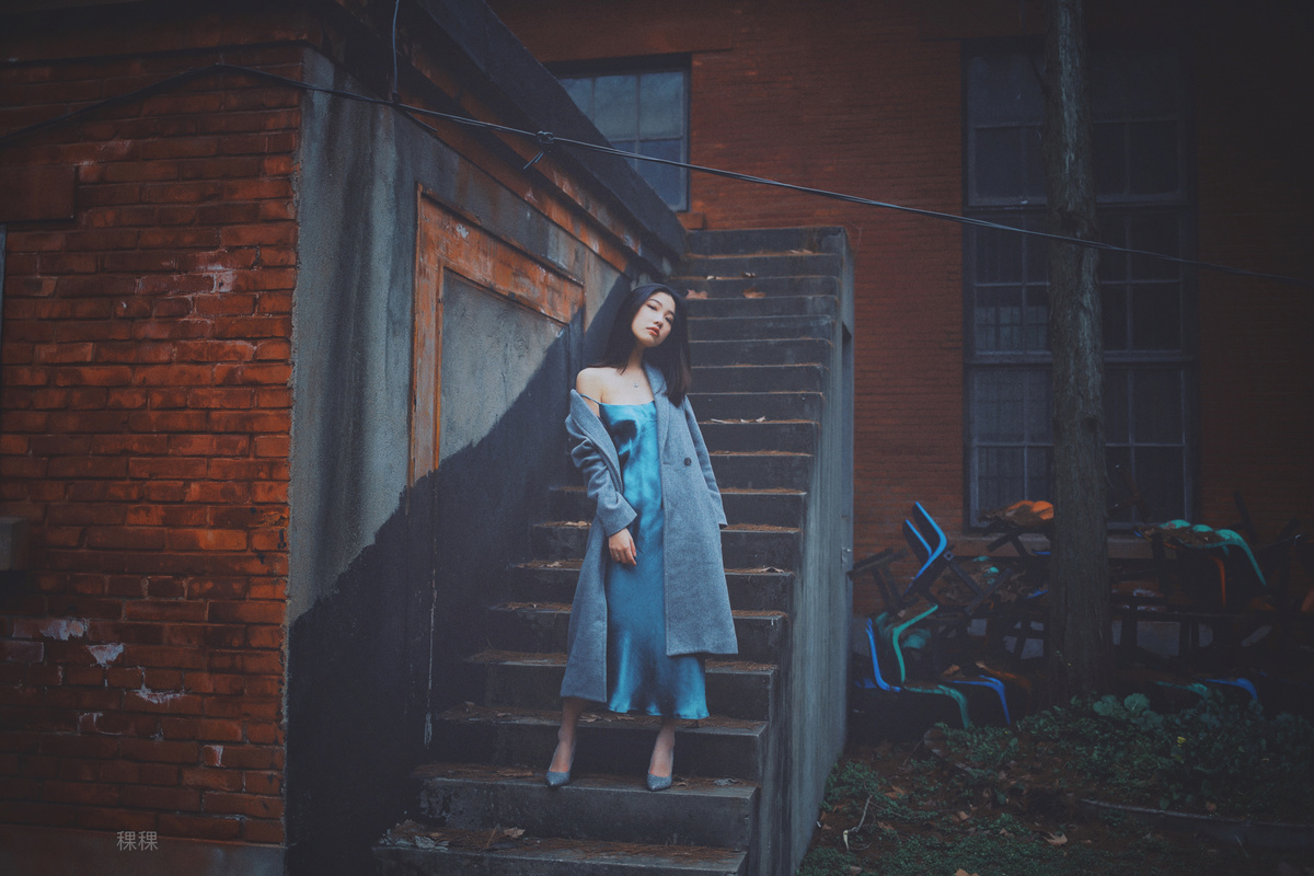 一个穿着蓝色连衣裙和外套的女人站在一所房子的台阶上
