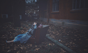 一个女人坐在地上有树叶的黑暗长椅上 一个人躺在椅子上