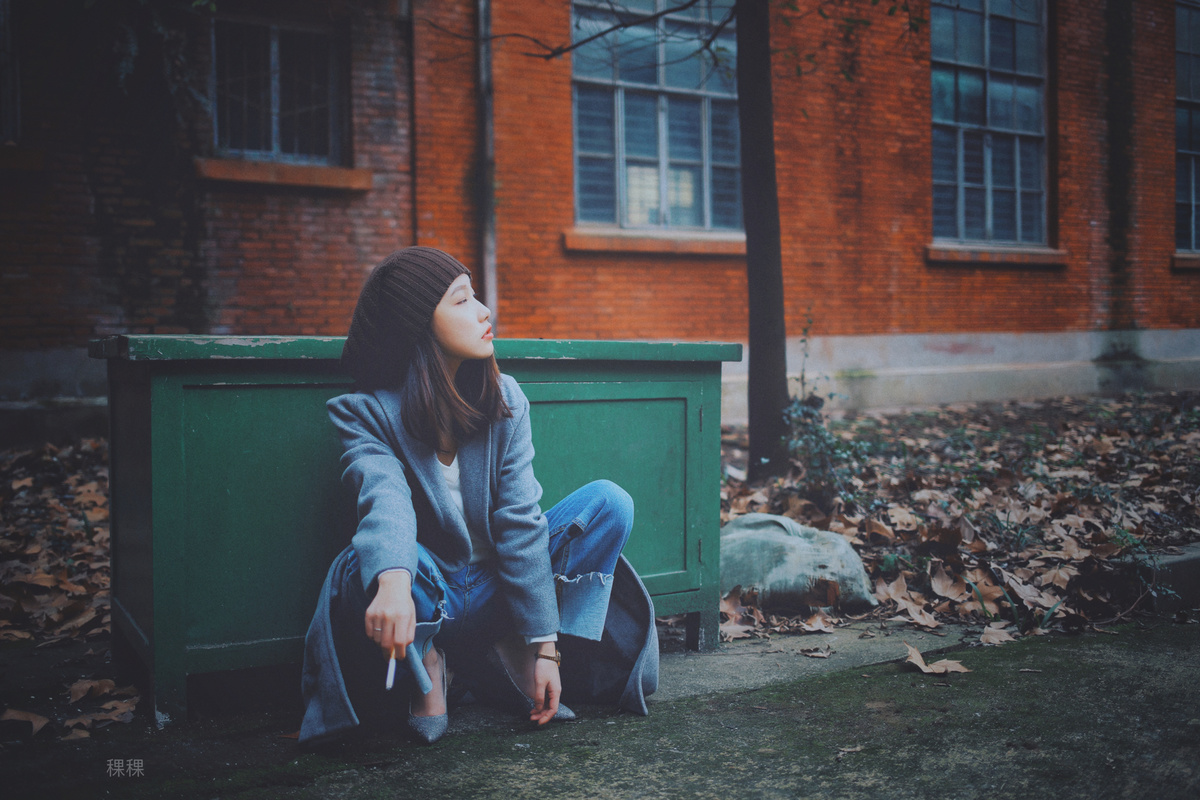 一位年轻女子坐在一座砖砌建筑前的绿色长椅上