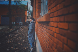 一个穿着外套的年轻女子站在砖墙和火车轨道旁的小巷里