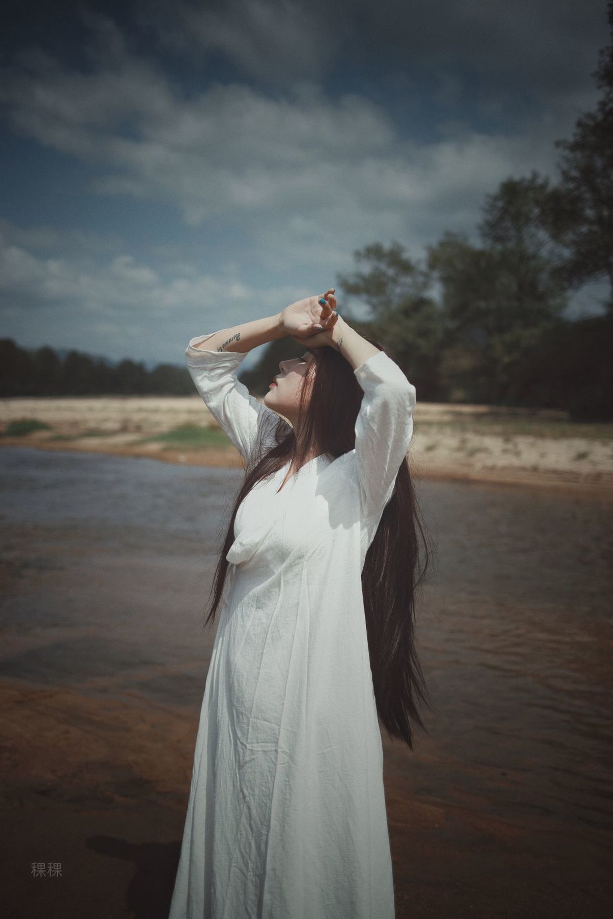 一位长发女孩穿着白色连衣裙站在海滩附近的水边