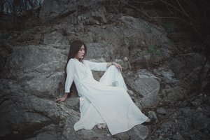 一位穿着长白色裙子的美女靠近岩石。