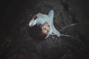 一个穿着白色连衣裙的年轻女子躺在洞穴中的一块岩石上