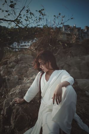 一位穿白色连衣裙的女子在岩石海滩上