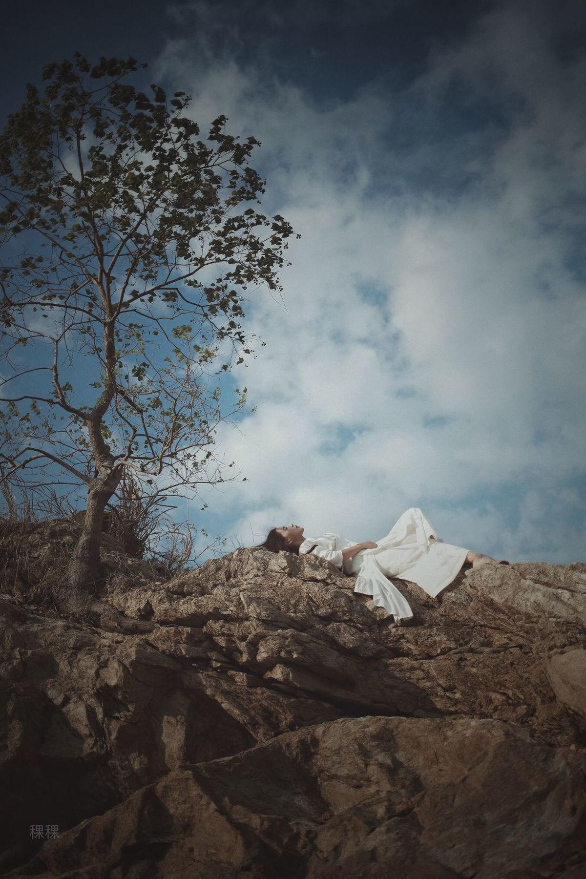 一个男子或女子躺在悬崖上 旁边有一棵树和天空 还有一个人在岩石上躺着。