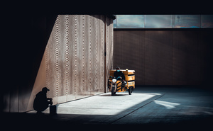 一个黑暗的房间 一个男人坐在建筑物的一侧 一辆黄色的摩托车停在阴影中。