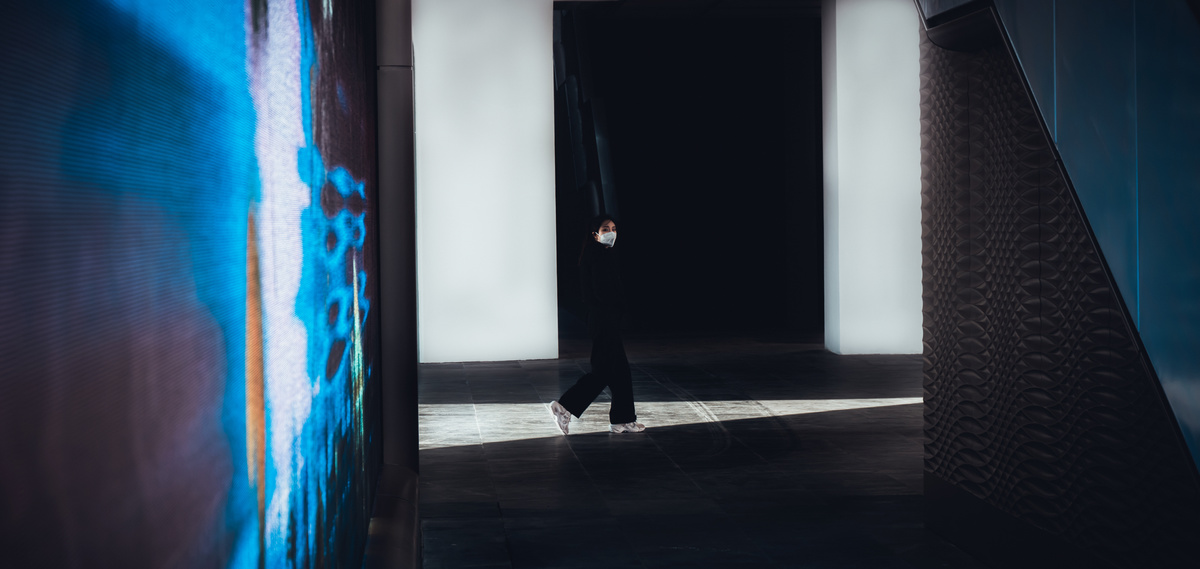 一个人走下黑暗的走廊 墙上有一个蓝色的灯 建筑物的门站着一个人。