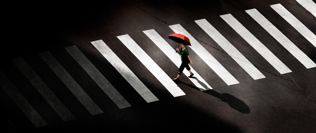 一个人在晚上穿越人行横道 带着红伞。