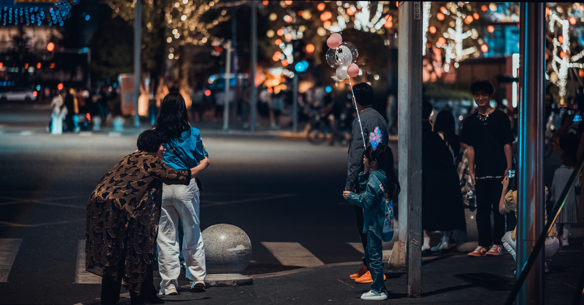 一个男子、一个女子和一个孩子站在夜晚街道的人行道上。