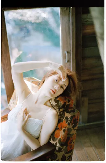 一个穿着白色连衣裙的女人坐在木椅上 面前有一扇窗户。