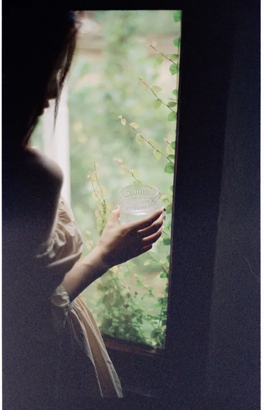 一位女士拿着一个玻璃窗 凝视着窗外的花。