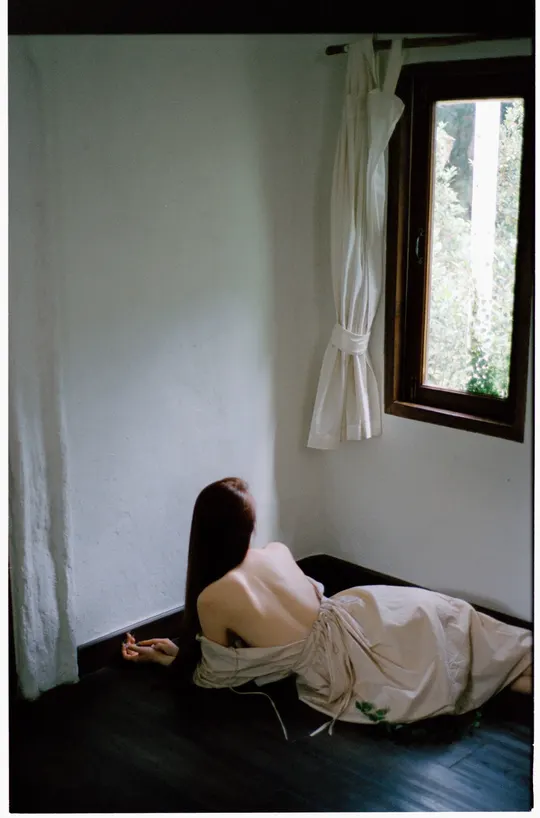 一个穿着白色连衣裙的年轻女子坐在房间的角落里 靠近窗户。