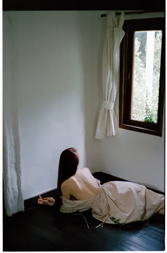 一个穿着白色连衣裙的年轻女子坐在房间的角落里 靠近窗户。