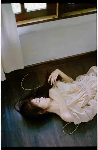 一个穿着白色连衣裙的年轻女子躺在有窗户的房间里地板上