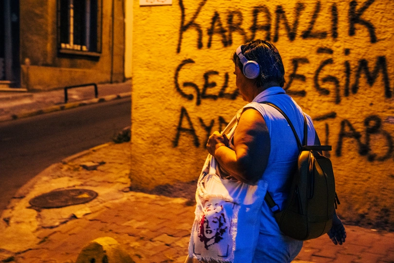 一位女士边走边听手机上的音乐 一位男士站在有涂鸦的墙前。