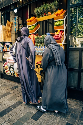 一些穿着穆斯林服装的女性走在水果和食物商店前的人行道上。
