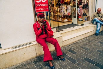 一位妇女坐在人行道上的一家商店前的墙边的长椅上 而一位男子正在使用他的手机。