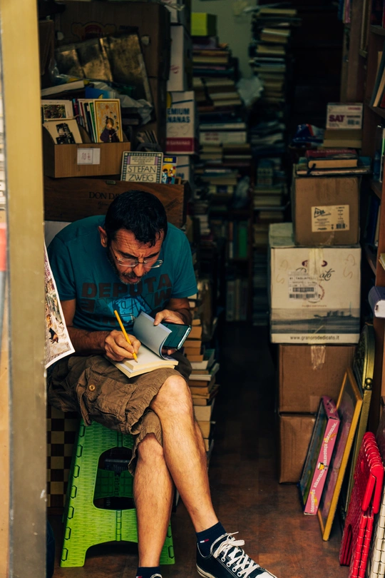 一个坐在杂物堆满的房间里阅读一本书并写笔记的人