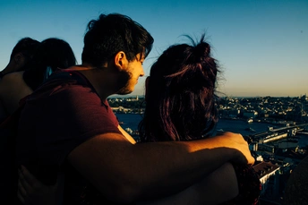 夕阳下 城市顶部的一个年轻男子和女子相拥。