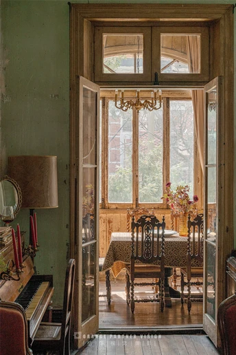 一个带有桌子、椅子、钢琴、吊灯和通向房子的门的房间。