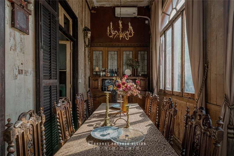 一张长餐桌和椅子 位于一所老房子里 有大型窗户 桌子上有一束花。