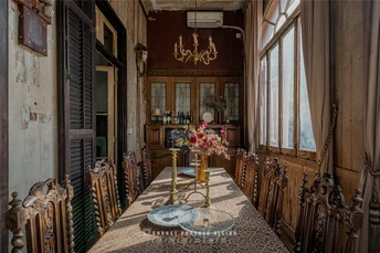 一张长餐桌和椅子 位于一所老房子里 有大型窗户 桌子上有一束花。