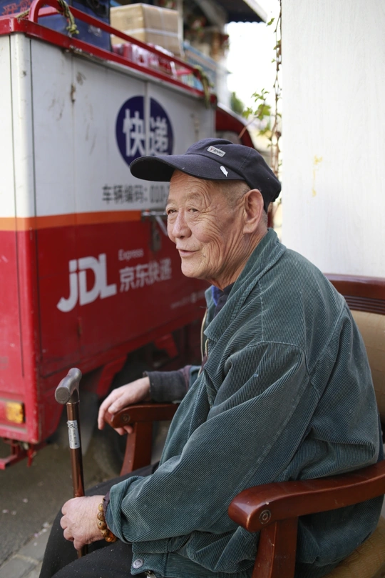 一位老人戴着帽子 手杖坐在红色卡车前面的椅子上。