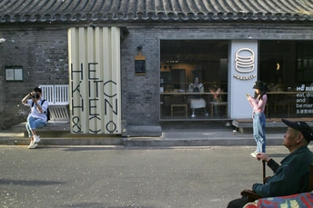 一位男士坐在路边的长椅上 一位女士在建筑物前拍摄街道。