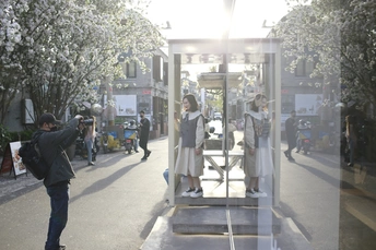 一个人站在滑板上人行道上 正在给人行道上行走的人们和公交车站拍照。