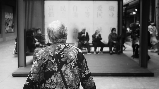 一张黑白照片 一位穿着和服的老妇人走在繁忙的街道上 周围有人们站立。