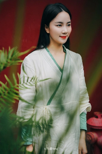 一位身穿白色和服、身穿绿色长袍的年轻女子站在红底前