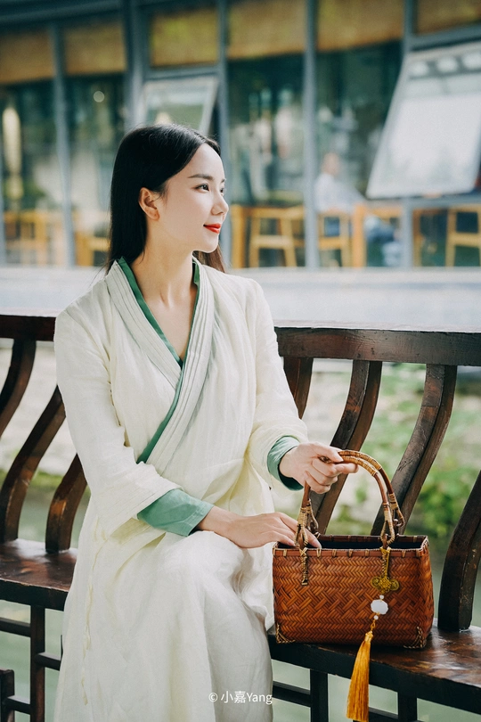 一个穿着白色连衣裙、拿着钱包的年轻女子坐在长椅上