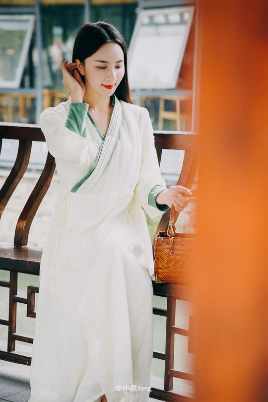 一个穿着白色长袍的年轻女子站在长椅旁