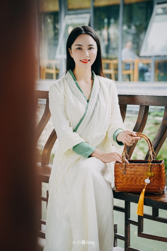 一个穿着白色长袍、拿着钱包的年轻女子坐在长椅上