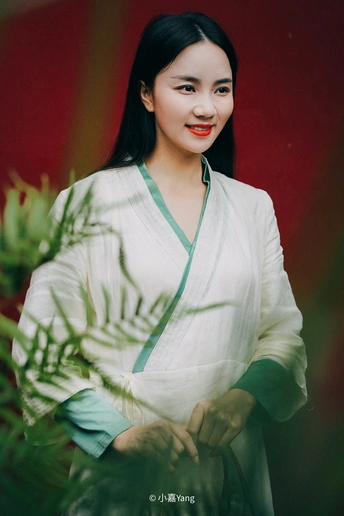 一名身穿白色连衣裙的年轻女子撑着绿色雨伞摆出姿势拍照