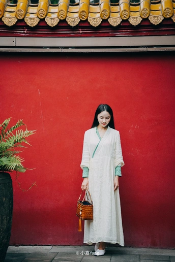 一位身穿白色连衣裙、拿着篮子的年轻女子站在红墙前