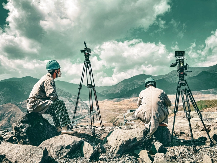 一个坐在岩石上的男人 带着相机和三脚架 正在给山脉拍照。