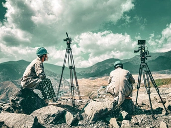 一个坐在岩石上的男人 带着相机和三脚架 正在给山脉拍照。