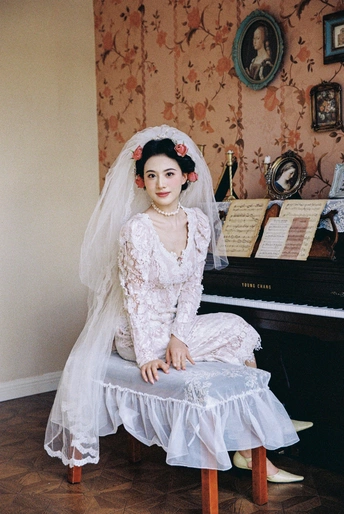 一个穿着白色连衣裙和面纱的年轻女子坐在钢琴前的椅子上