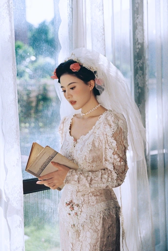 一位穿着白色婚纱的女人在窗前读书