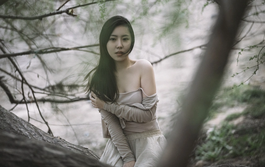 一位穿着白色连衣裙的年轻女子穿过一排树木和水边的森林。