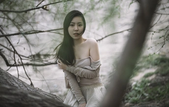 一位穿着白色连衣裙的年轻女子穿过一排树木和水边的森林。