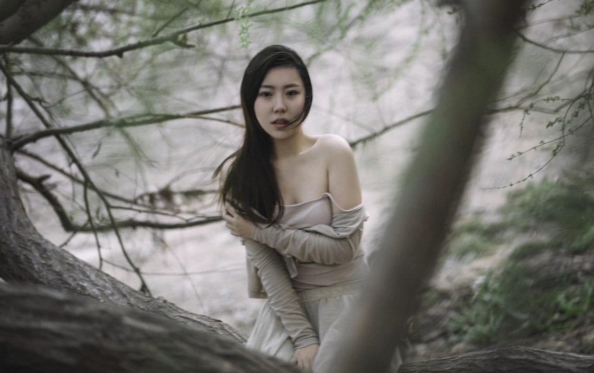 一位穿着白色连衣裙的年轻女子穿过一棵棵树的森林。