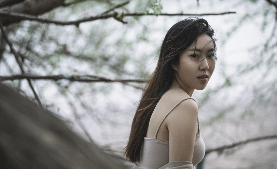 一个穿着白色连衣裙的年轻女子站在森林中 在伞下。