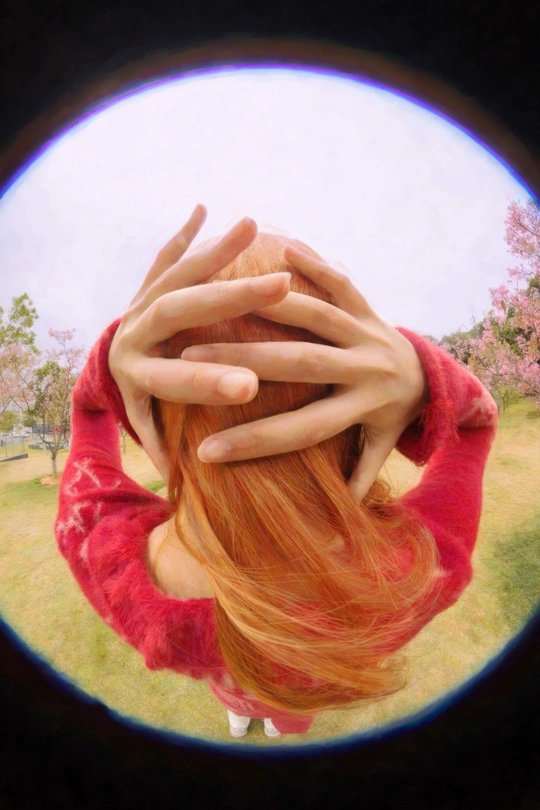 一个红头发的女孩用双手遮住脸颊 透过圆形窗户向外看。