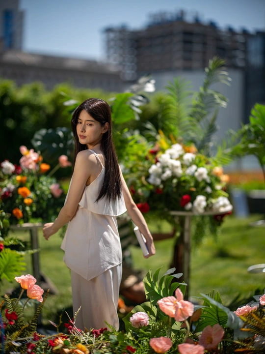 一位穿着白色连衣裙的年轻女子站在花园里 周围有花。