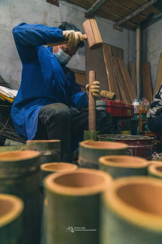 在一个工坊里工作的男子 手里拿着锤子 旁边放着一个放在木板上的花瓶。